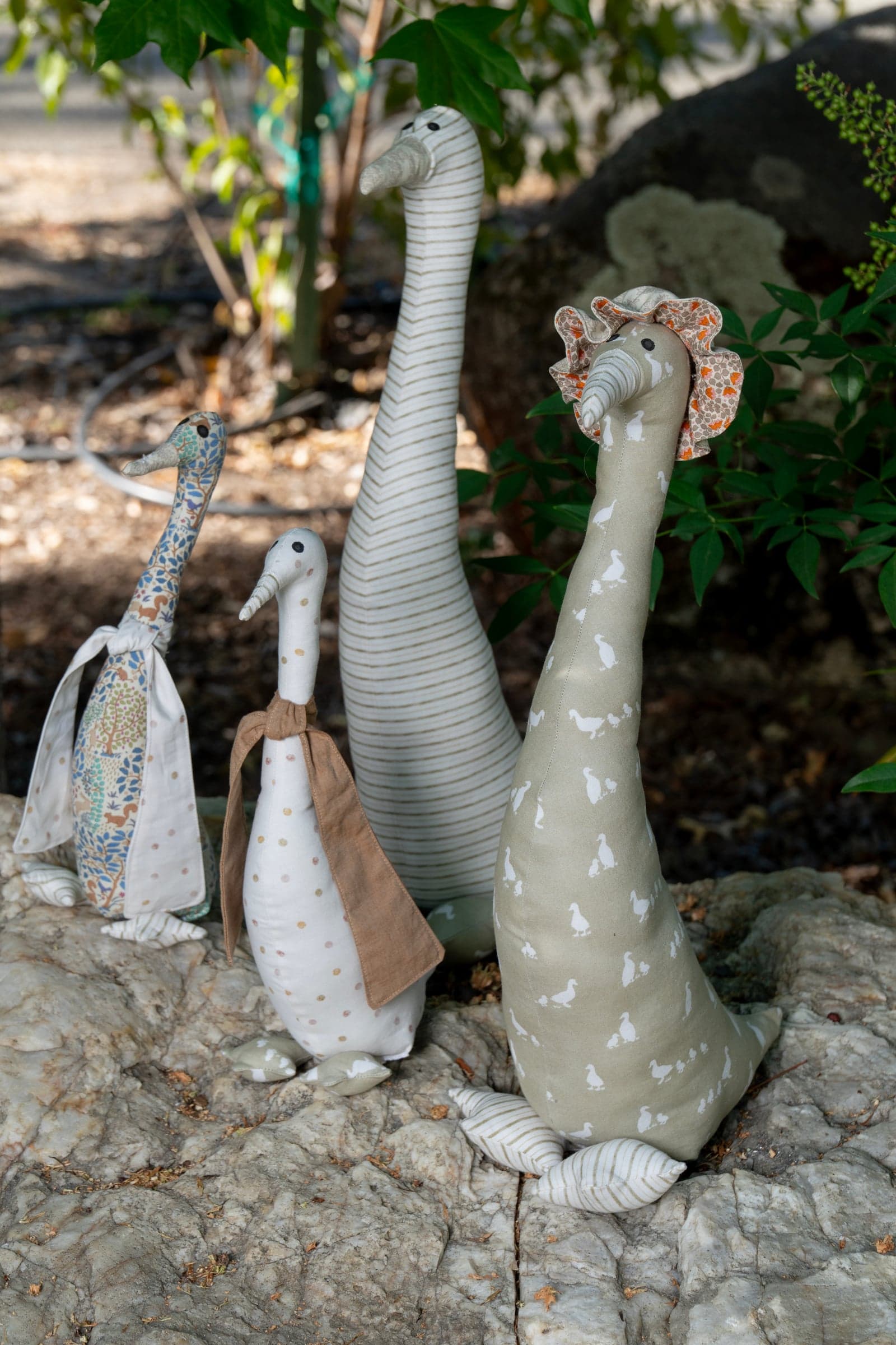 Four handmade fabric ducks in prints and stripes, two wearing little scarves, standing on a rock