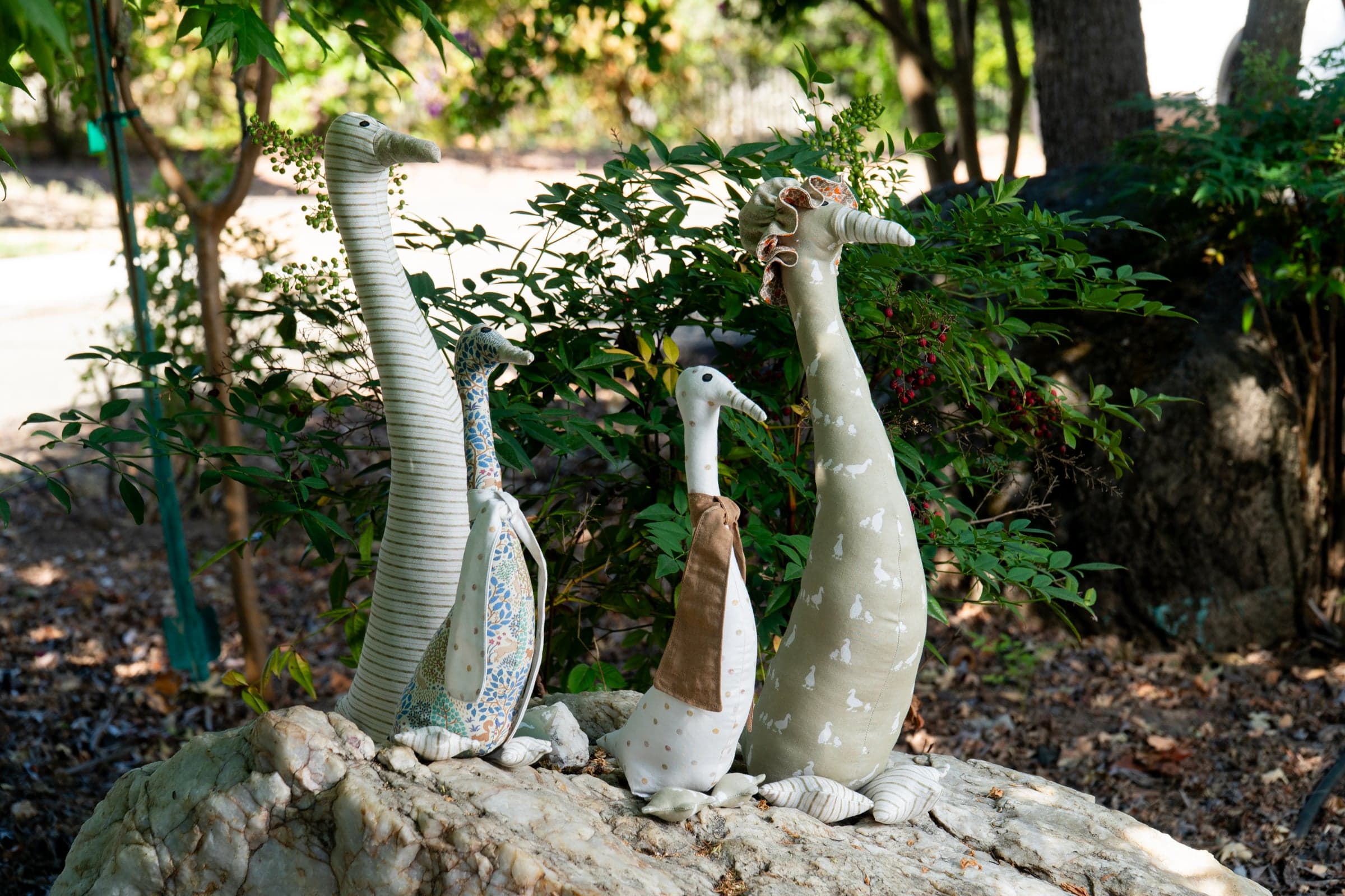 The fabric ducks lined up together on a rock in the garden