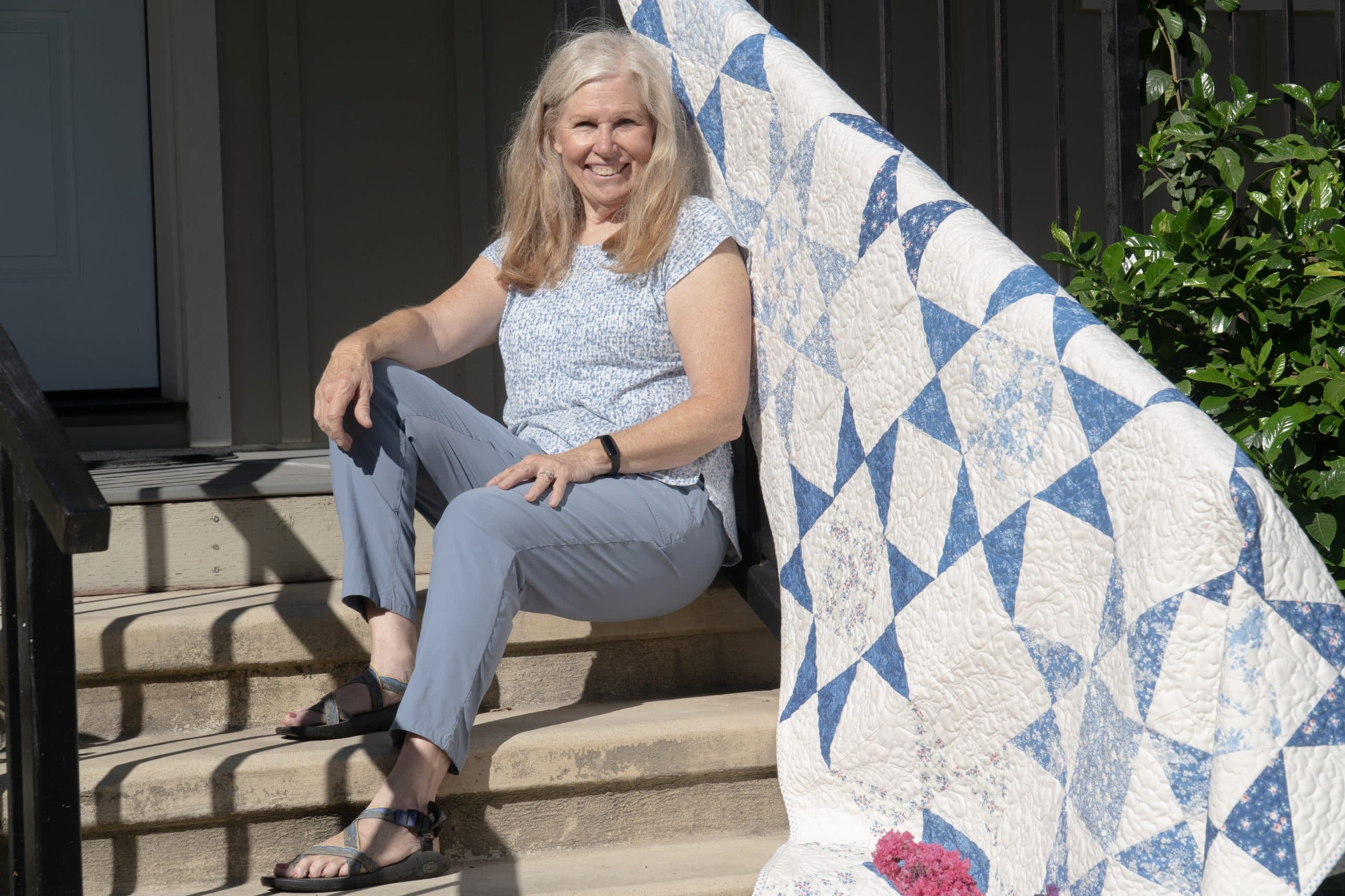 The quilter, seated on a porch step beside one of her finished quilts