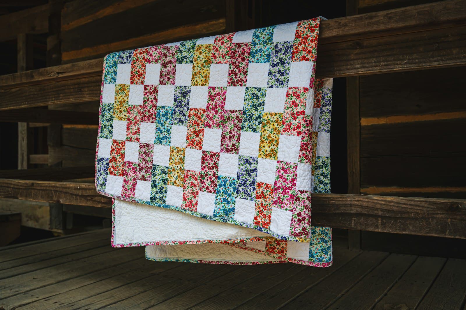 Green and cream checkered quilt draped over a wooden railing